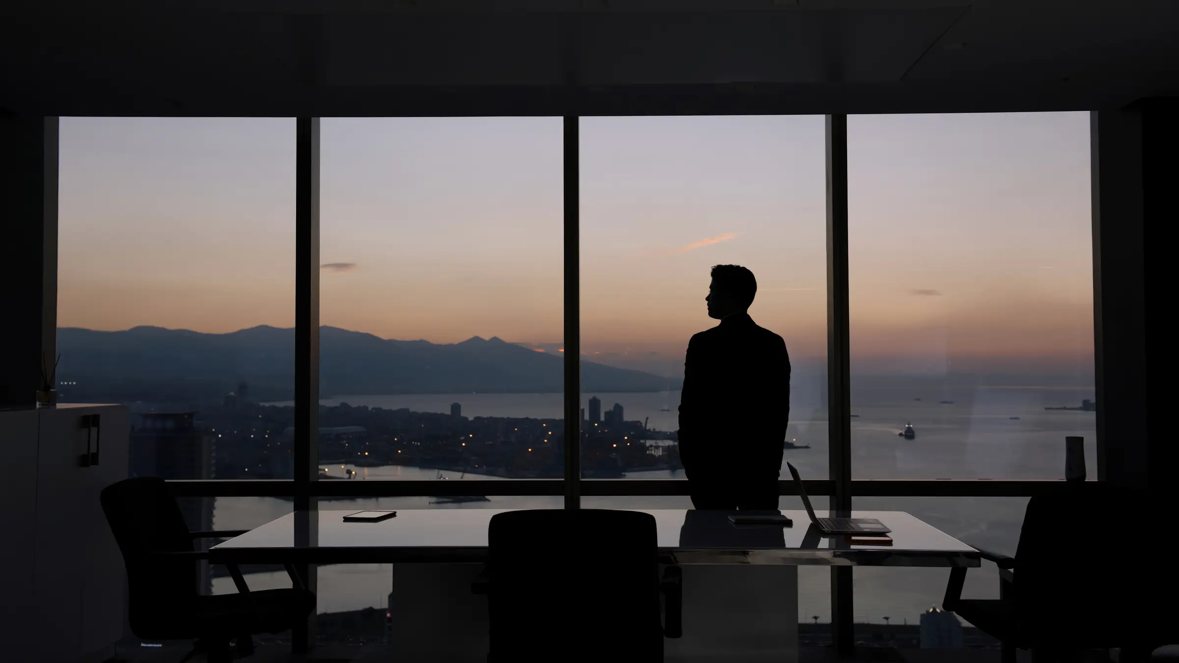 An advisor looks out over the harbor from a high-rise office at dawn.
